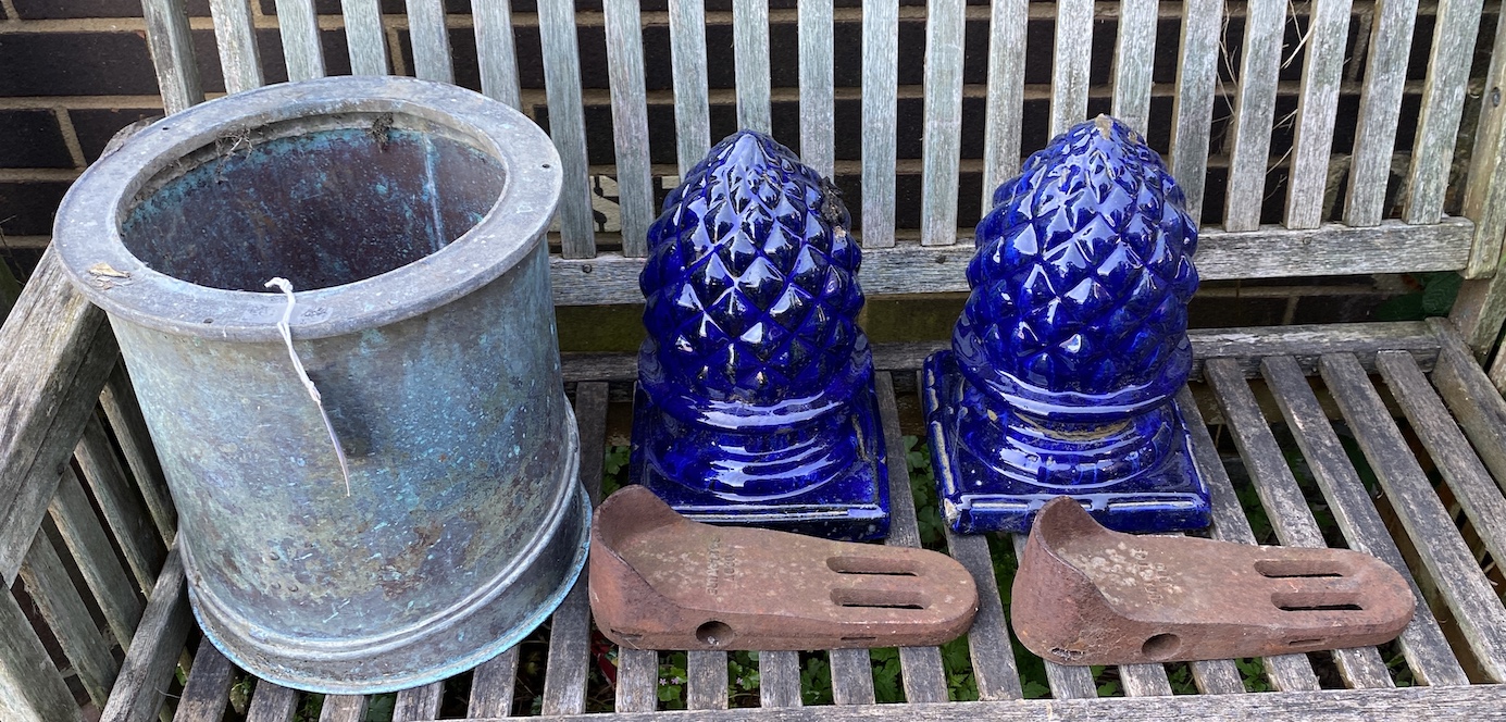 A circular copper container, diameter 31cm, a pair of diver's boots weights and two glazed pottery pineapple finials